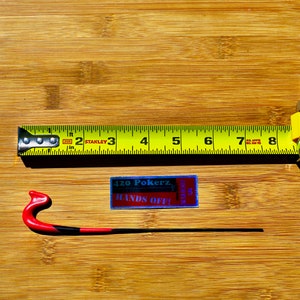 Puede incluir: Una cinta métrica amarilla con marcas negras y una caja plateada. La cinta dice "Stanley" y tiene marcas para pulgadas y pies. También se ve un gancho rojo y negro. Un adhesivo con el texto "420 Pokerz Hands Off!" es visible.