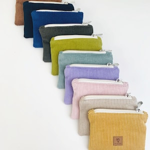 May include: A set of ten small zippered pouches in various colors, including brown, blue, green, yellow, and purple. The pouches are made of corduroy fabric and have a small heart-shaped logo on the front.