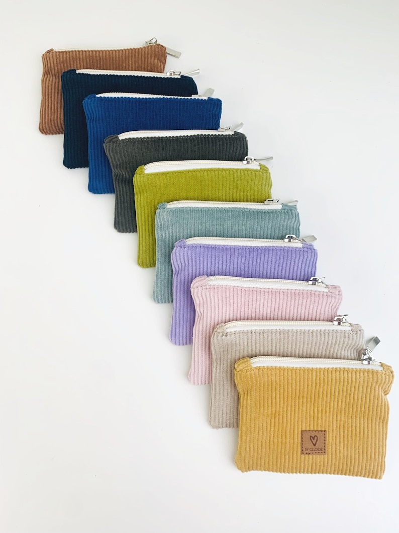 May include: A set of ten small zippered pouches in various colors, including brown, blue, green, yellow, and purple. The pouches are made of corduroy fabric and have a small heart-shaped logo on the front.