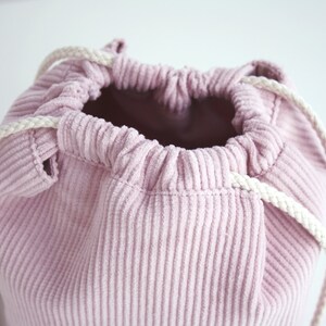 Puede incluir: Una bolsa de cord&oacute;n de pana rosa con cordones blancos. La bolsa est&aacute; hecha de una tela suave y texturizada y tiene una abertura ancha.