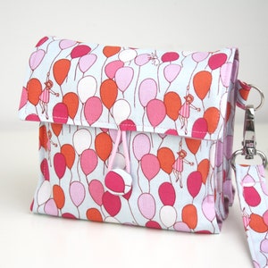 Può includere: Una piccola borsa di tessuto blu con una stampa di palloncini rosa e arancioni. La borsa ha una chiusura a lembo con un cordoncino rosa e una tracolla rimovibile.