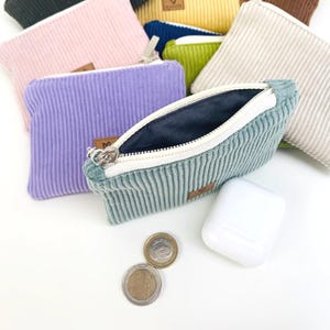 May include: A set of small zippered pouches made of corduroy fabric in various colors, including pink, purple, green, beige, and blue. The pouches are open to show the soft, plush lining inside.