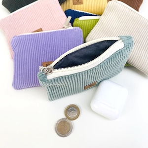 May include: A set of small zippered pouches made of corduroy fabric in various colors, including pink, purple, green, beige, and blue. The pouches are open and show the soft, textured fabric lining.