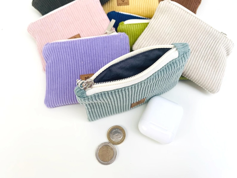 May include: A set of small zippered pouches made of corduroy fabric in various colors, including pink, purple, green, beige, and blue. The pouches are open and show the soft, textured fabric lining.