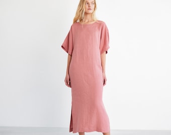 Puede incluir: Un vestido largo de lino rosa de corte holgado y mangas cortas. El vestido tiene un escote redondo y una abertura lateral.