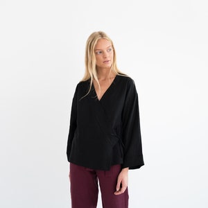 Op de afbeelding: Een zwart wikkeltop met lange mouwen en een V-hals. Het top is in de taille geknoopt en heeft een losse pasvorm.