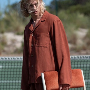 Könnte beinhalten: Ein rustfarbenes Leinenhemd und eine Shorts mit Knopfleiste und einer Brusttasche. Die Person hält einen Stuhl mit einem roten Samtsitz.