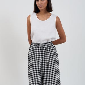 Puede incluir: Una camiseta sin mangas de lino blanco combinada con pantalones de pernera ancha a cuadros blancos y negros. Los pantalones tienen cintura elástica. El conjunto es sencillo e informal, adecuado para el uso diario.