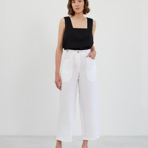 Peut inclure: Une femme portant un haut noir sans manches et un pantalon blanc en lin avec des poches. Elle porte des sandales beiges.