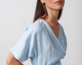 Puede incluir: Un vestido de lino azul claro con cuello en V y mangas cortas. El vestido tiene un cinturón de lazo en la cintura.