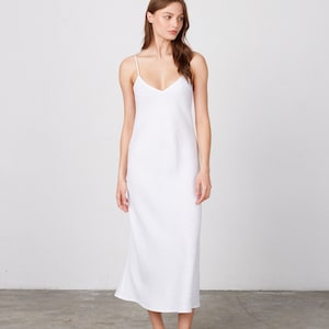 May include: A white sleeveless maxi dress with a V-neckline. The dress is made of a soft, flowing fabric and has a relaxed fit.