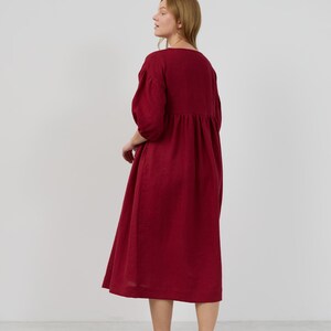 May include: A long, burgundy-colored dress with a gathered skirt and 3/4 sleeves. The dress is made of a lightweight fabric and has a relaxed fit.