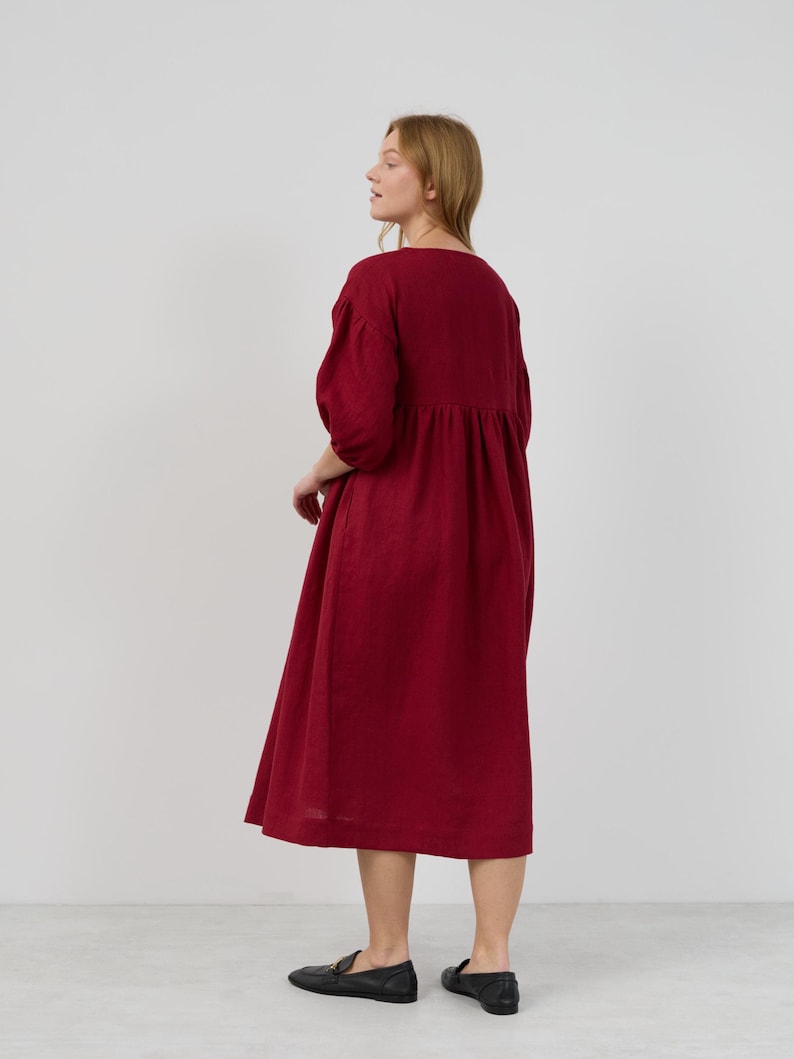 May include: A long, burgundy-colored dress with a gathered skirt and 3/4 sleeves. The dress is made of a lightweight fabric and has a relaxed fit.