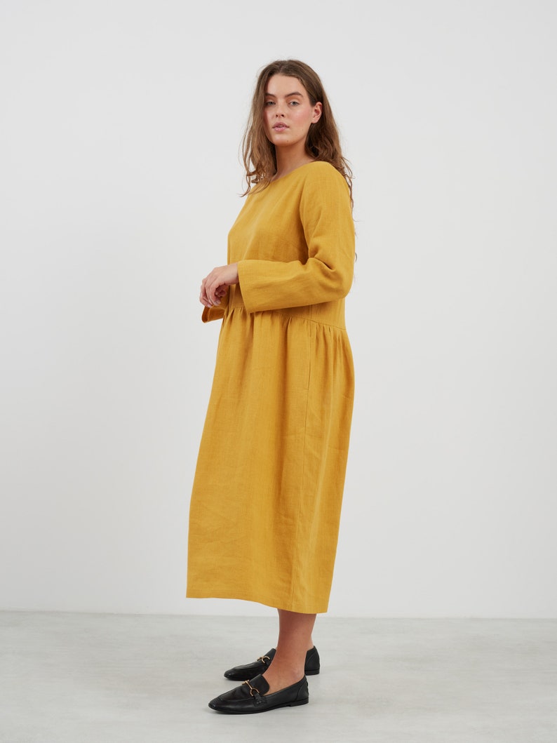 May include: A long-sleeved, mustard yellow linen dress with a gathered skirt and a round neckline.