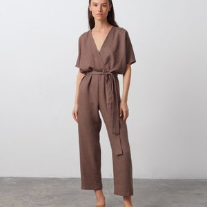 May include: A brown linen jumpsuit with a V-neckline, short sleeves, and a tie belt. The jumpsuit has a relaxed fit and a wide leg.