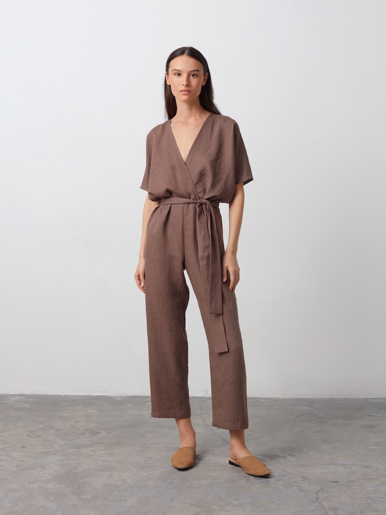 May include: A brown linen jumpsuit with a V-neckline, short sleeves, and a tie belt. The jumpsuit has a relaxed fit and a wide leg.