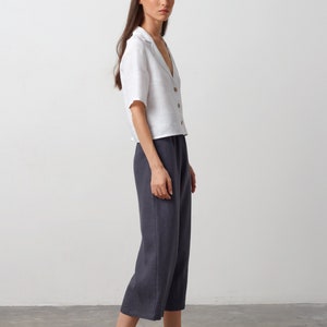 May include: A woman wearing a white linen shirt with a collar and a pair of dark gray linen pants. She is wearing black leather slip-on shoes.
