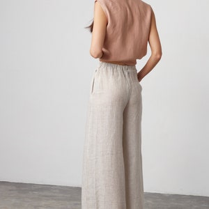Pu&ograve; includere: Un paio di pantaloni di lino a gamba larga con strisce, vita alta e vestibilit&agrave; rilassata. I pantaloni sono di colore beige chiaro con sottili strisce marroni.