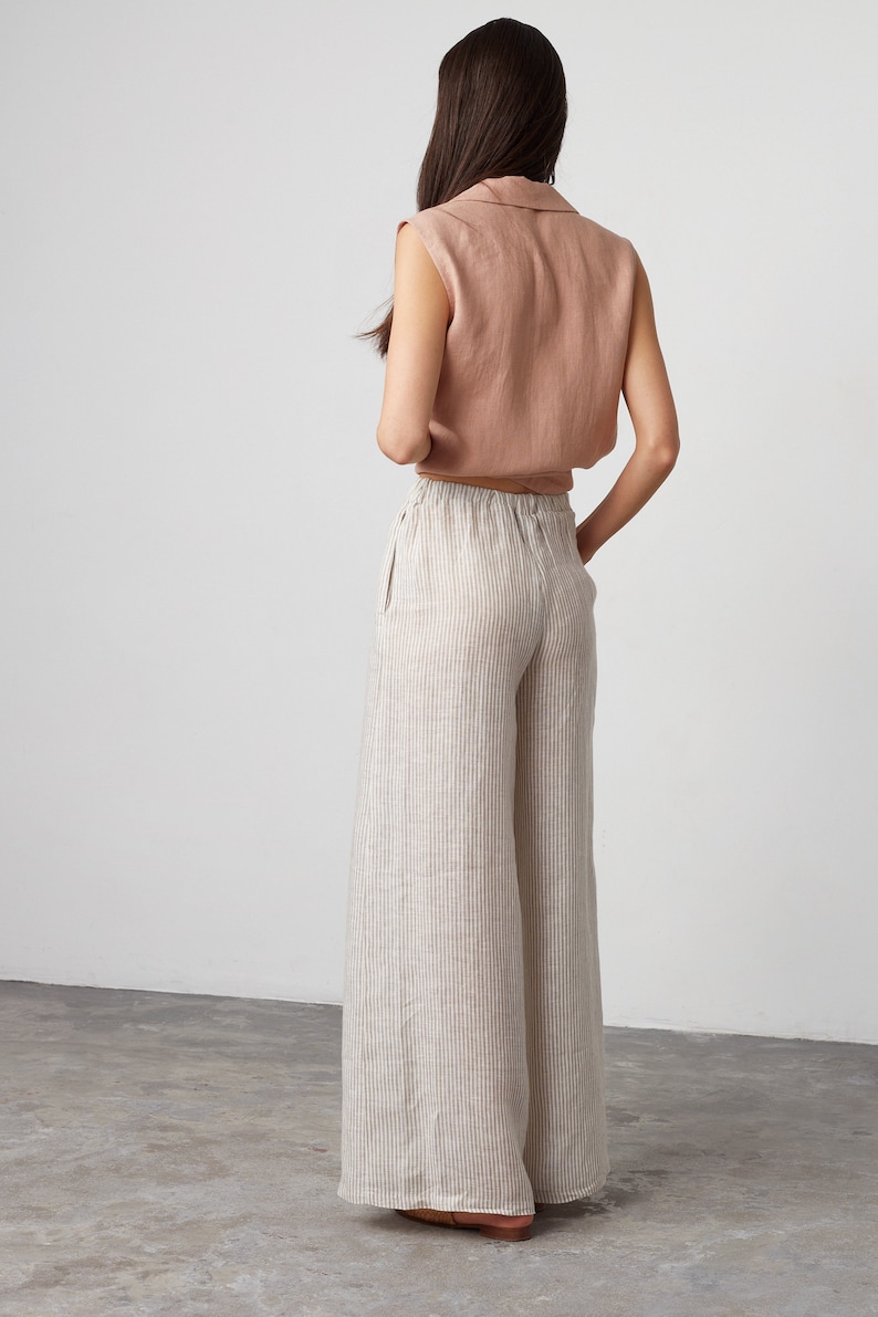 Pu&ograve; includere: Un paio di pantaloni di lino a gamba larga con strisce, vita alta e vestibilit&agrave; rilassata. I pantaloni sono di colore beige chiaro con sottili strisce marroni.
