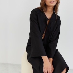 May include: A black long-sleeved dress with a tie at the neckline. The dress has a relaxed fit and a midi length.