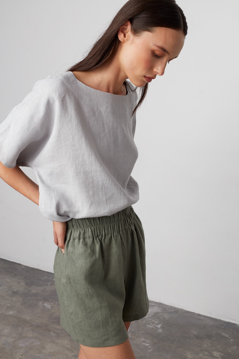 Pode incluir: Uma mulher vestindo uma blusa de linho cinza claro e shorts de linho verde oliva. Os shorts t&ecirc;m uma cintura el&aacute;stica.
