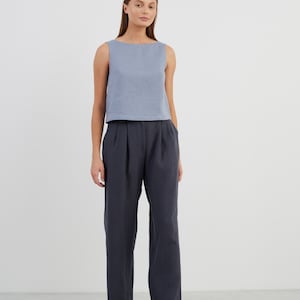 May include: A woman is wearing a light blue sleeveless linen top and dark blue linen trousers. She is wearing black loafers with gold buckles.