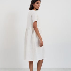 Side-back view of the DOVE linen midi dress in Ivory showing the short sleeve, gathered waist seam, and midi-length skirt