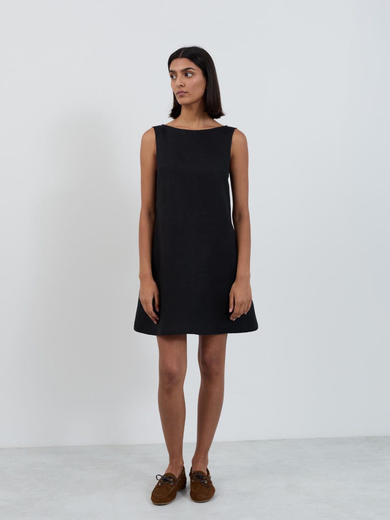 Full-length front view of the CECILIA Black linen mini dress showing the clean boat neckline and A-line shape falling above the knee