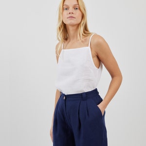 May include: A white linen tank top with a square neckline and a pair of dark blue linen pants with pleats. The pants have a high waist and a wide leg.