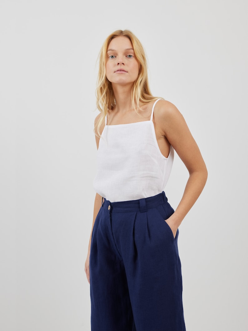 May include: A white linen tank top with a square neckline and a pair of dark blue linen pants with pleats. The pants have a high waist and a wide leg.