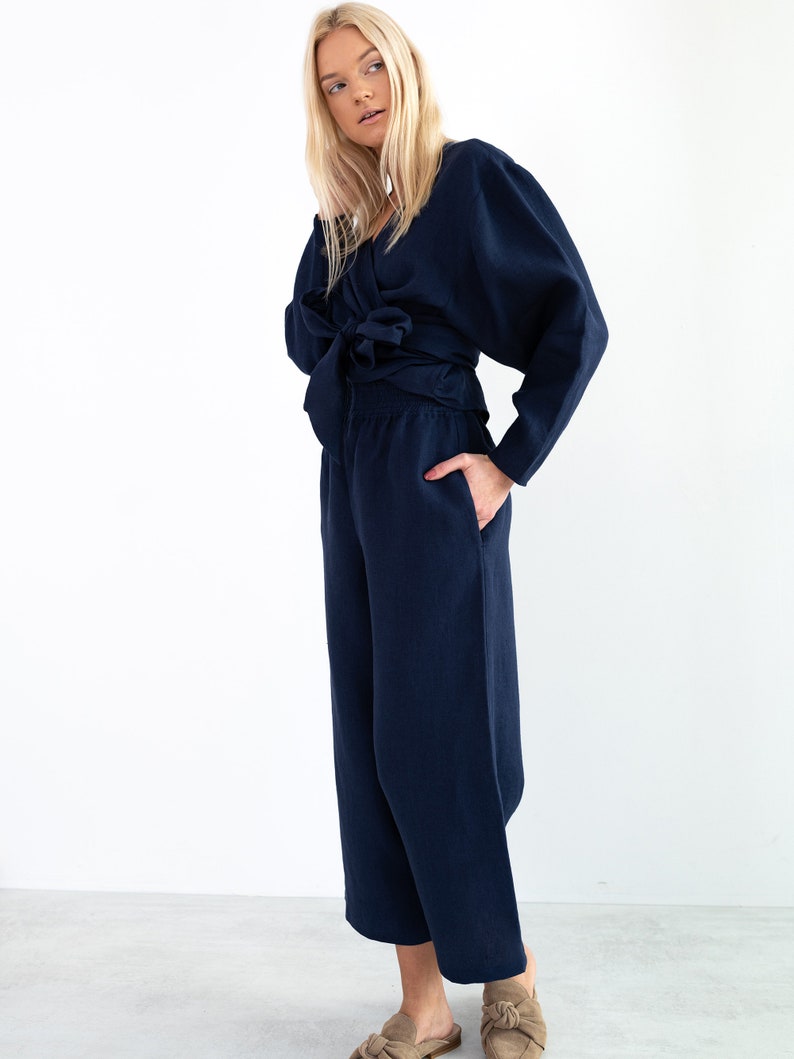 May include: A navy blue linen wrap top with long sleeves and a tie at the waist, paired with matching wide-leg pants.