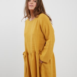 May include: A long-sleeved, yellow linen dress with a round neckline and a gathered skirt. The dress has two pockets on the sides.