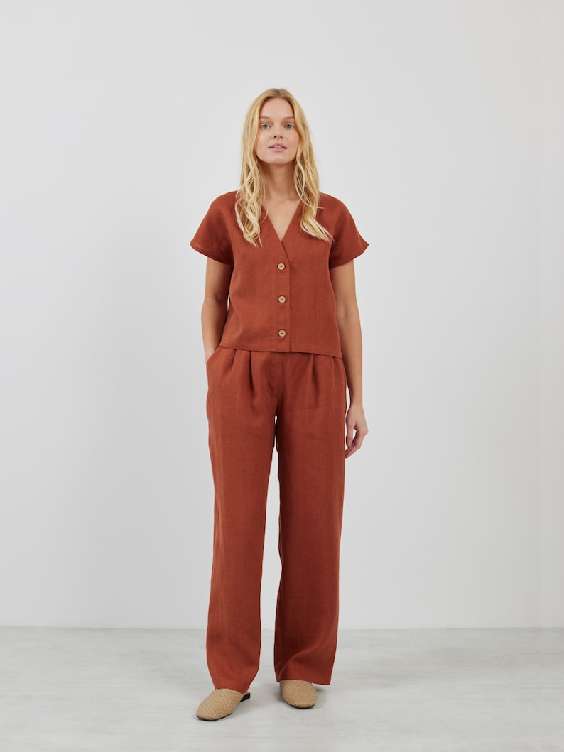 May include: A rust-colored linen top with a v-neck and short sleeves, paired with matching wide-leg linen pants. The top has a button-up front.