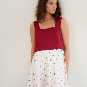 Puede incluir: Una mujer lleva un top de tirantes de lino rojo con escote cuadrado y una falda blanca con estampado de cerezas.