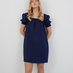 Op de afbeelding: Een kort, donkerblauw jurkje met een vierkante halslijn en een geplooide taille.