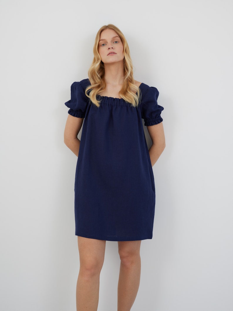 Op de afbeelding: Een kort, donkerblauw jurkje met een vierkante halslijn en een geplooide taille.