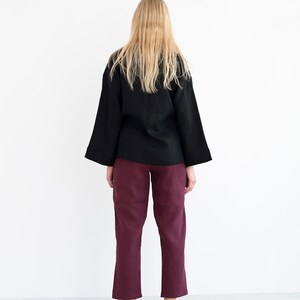 Op de afbeelding: Een zwart linnen top met lange mouwen en een bordeauxrode linnen broek.