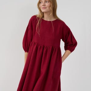 May include: A burgundy midi dress with a round neckline and 3/4 sleeves. The dress has a gathered waist and a flowy skirt.
