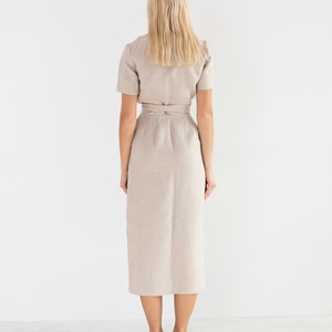 May include: A beige linen dress with a wrap style and a tie belt. The dress has short sleeves and a midi length.