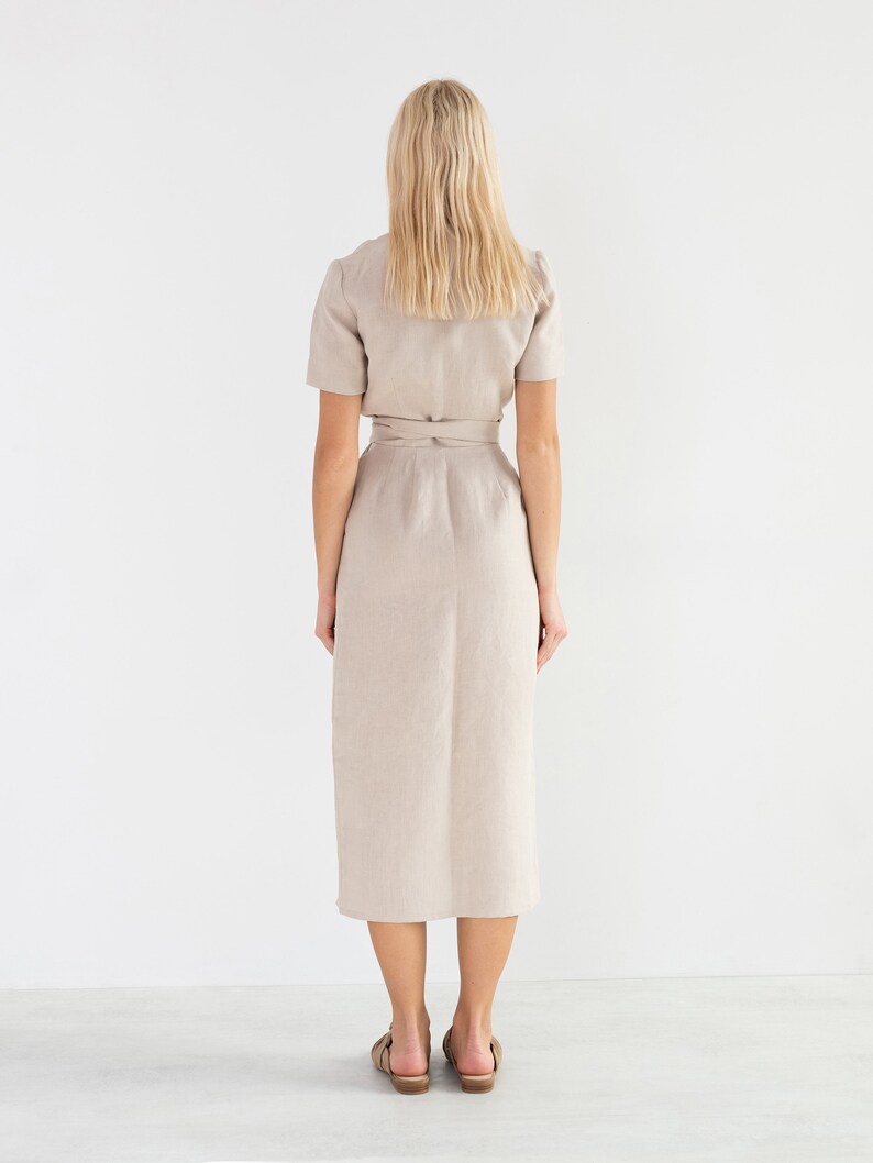May include: A beige linen dress with a wrap style and a tie belt. The dress has short sleeves and a midi length.