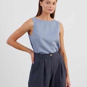 May include: A woman wearing a light blue sleeveless top and dark grey wide-leg trousers. The trousers have a button fastening and pleats at the front.