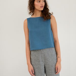 May include: A woman wearing a blue sleeveless top and black and white checked trousers.