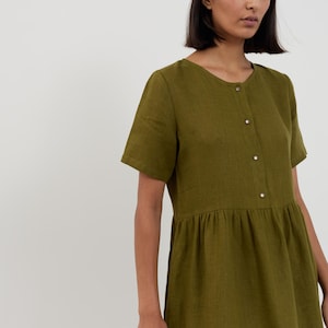 Close-up of the SAGE dress bodice showing round neckline, short sleeves, and metal snap button closure on Moss Green linen