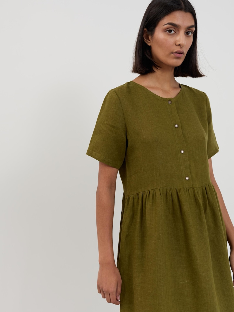 Close-up of the SAGE dress bodice showing round neckline, short sleeves, and metal snap button closure on Moss Green linen