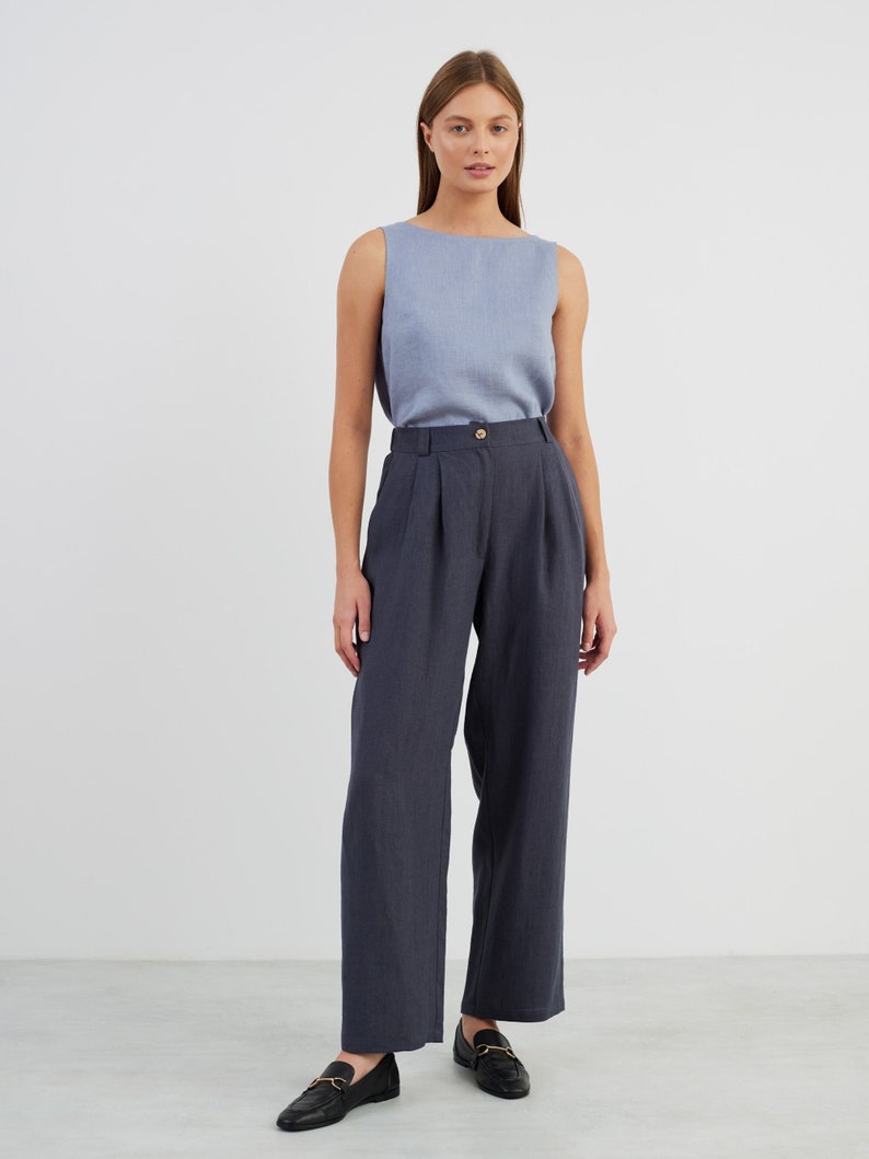 May include: A woman is wearing a light blue sleeveless top and dark blue wide-leg trousers. She is wearing black loafers with gold buckles.