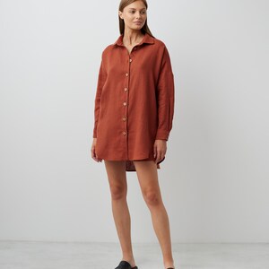 May include: A rust-colored linen shirt dress with long sleeves and a button-down front. The dress is loose-fitting and falls to the mid-thigh.
