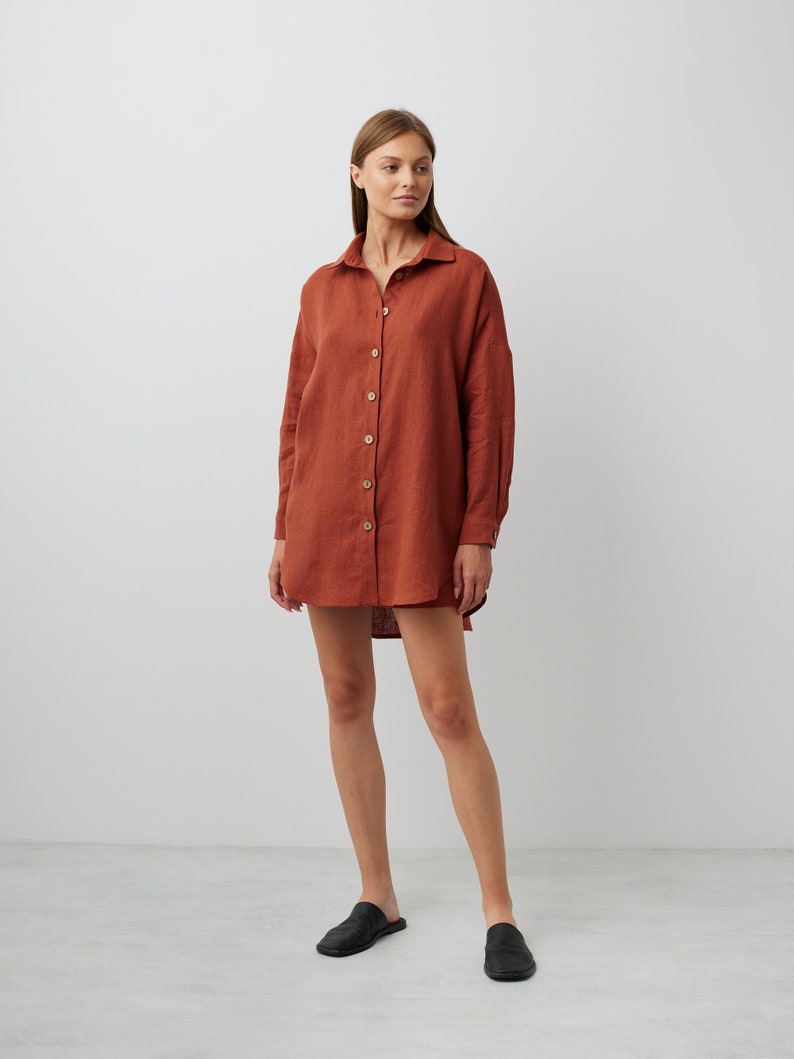 May include: A rust-colored linen shirt dress with long sleeves and a button-down front. The dress is loose-fitting and falls to the mid-thigh.
