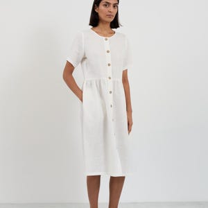 Full-length front view of the DOVE Ivory linen midi dress with hand resting in side seam pocket showing the relaxed gathered-waist silhouette