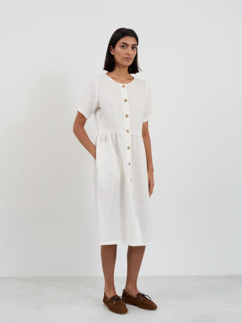 Full-length front view of the DOVE Ivory linen midi dress with hand resting in side seam pocket showing the relaxed gathered-waist silhouette