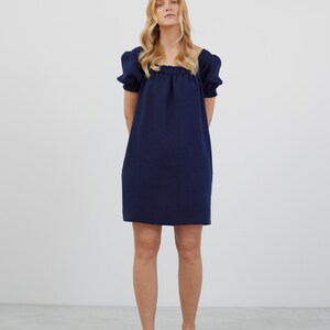 Op de afbeelding: Een kort, donkerblauw jurkje met een vierkante halslijn en een geplooide taille.